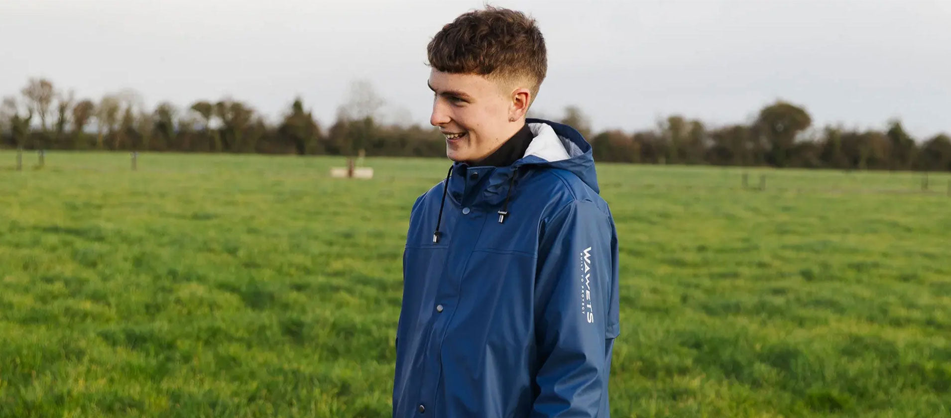 "Man in fields happy wearing Wawets navy/blue waterproof tcoat with zip pocket & hood"