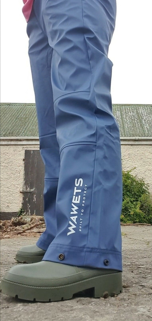 A person wearing Wawets blue waterproof pants which are breathable standing on a concrete surface with a farmshed in the background.