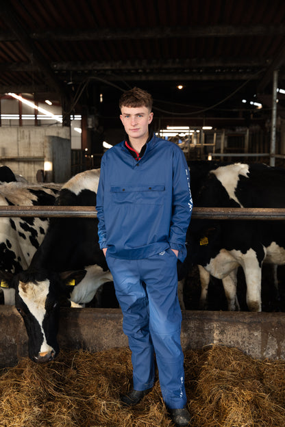 A person wearing a blue waterproof dairy top with Velcro fasteners standing in front of cows in a barn.